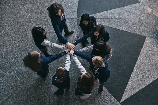kolorowe zdjęcie: dziewięcioro studentów ubranych w ciuchy z logo UŚ, stojących w kręgu i robiących gest wzajemnego wsparcia